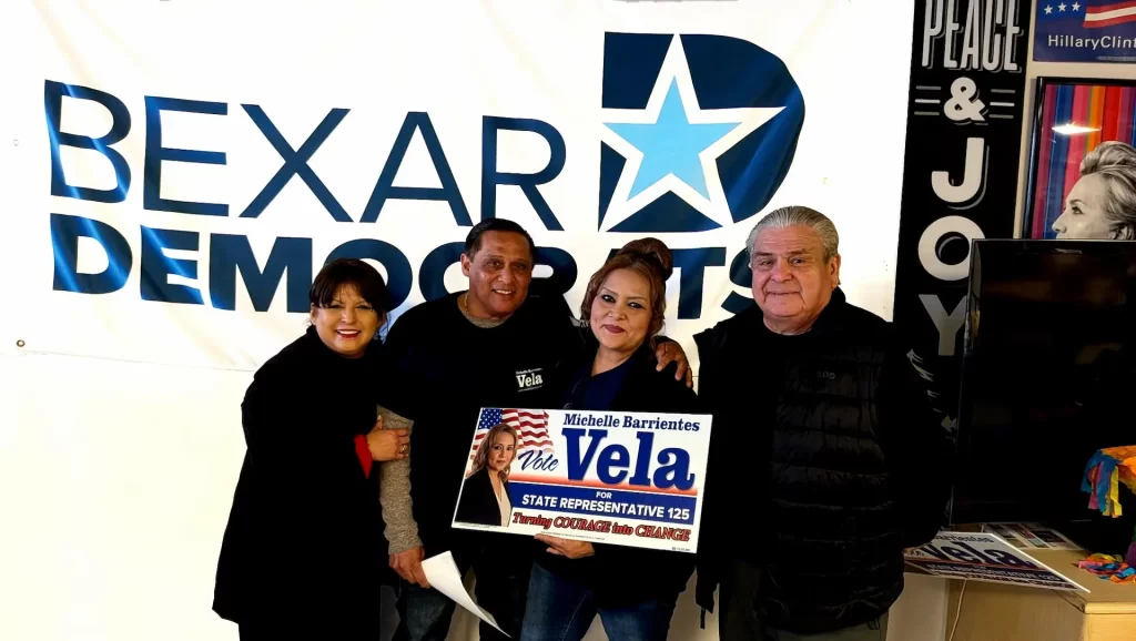 Michelle Barrientes Vela at Bexar Democrats headquarters with husband Carlos Vela, Norma Villareal, and Juan Hernandez holding a campaign flyer.